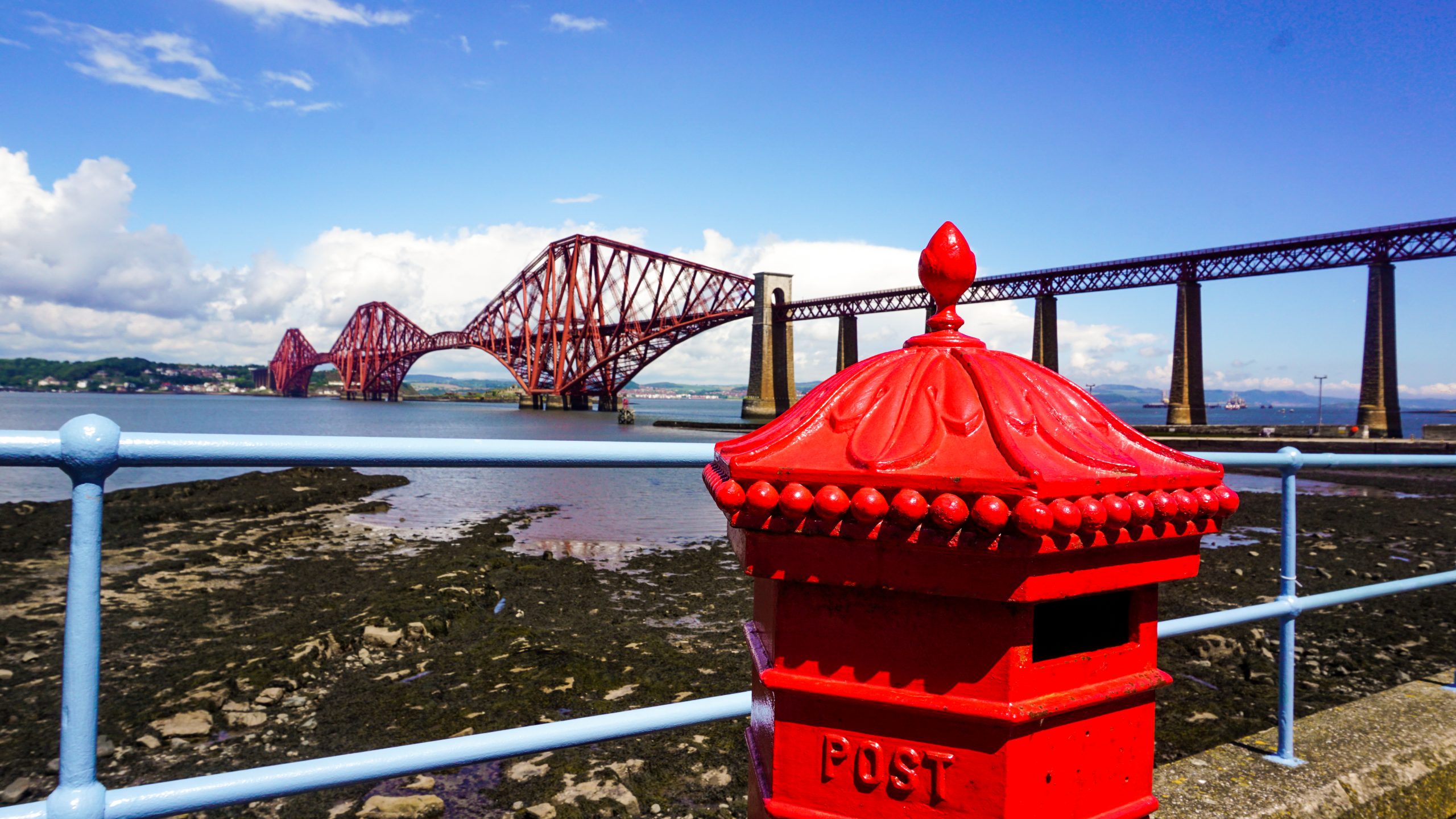 A red post box in front of the Forth Bridge