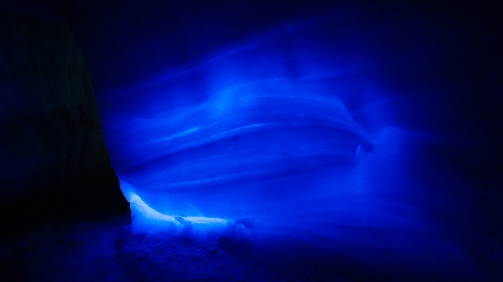 The side of an ice cave lighted with blue artificial light