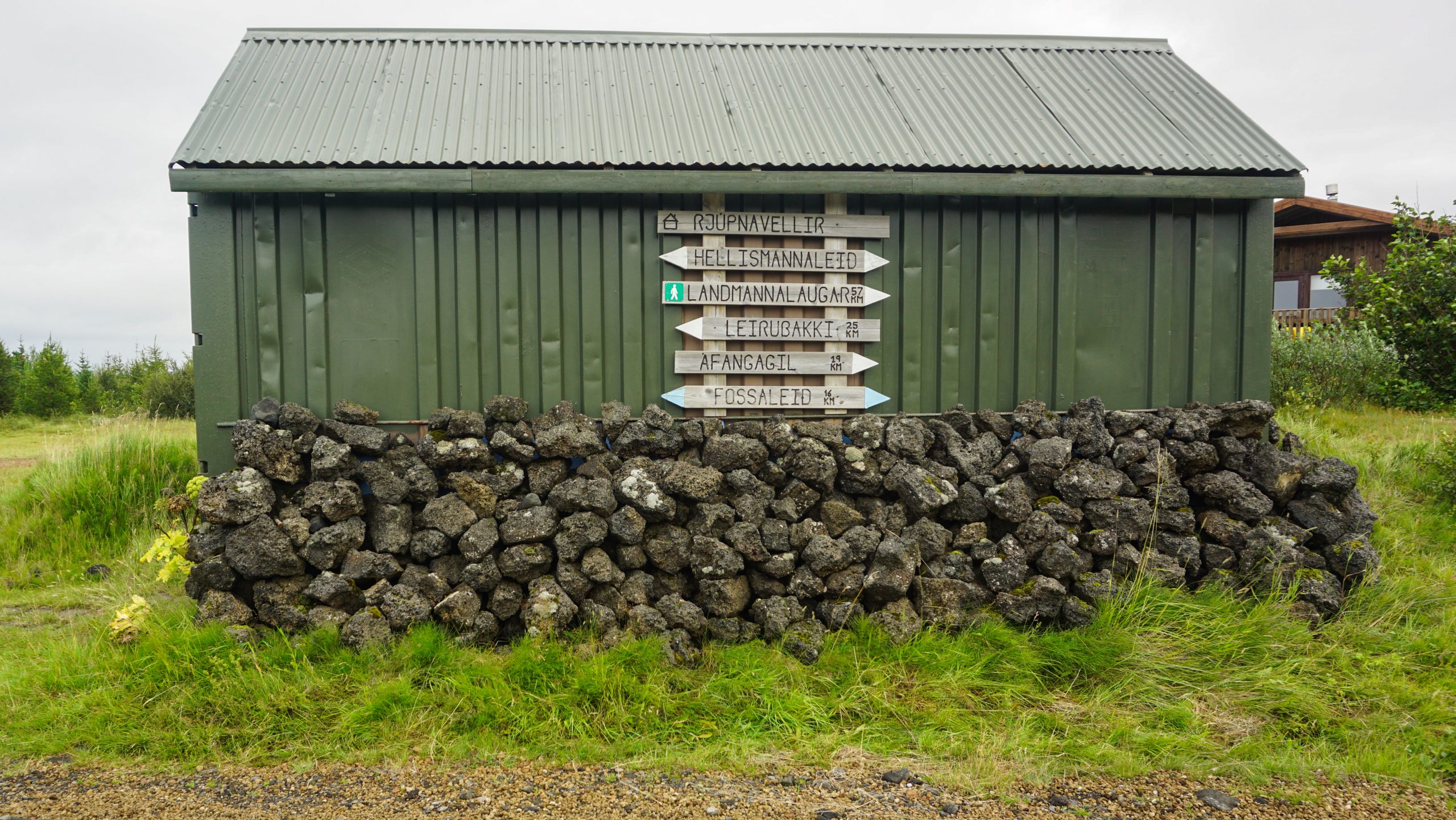 A green hut with a sign for directions of different routes in the area