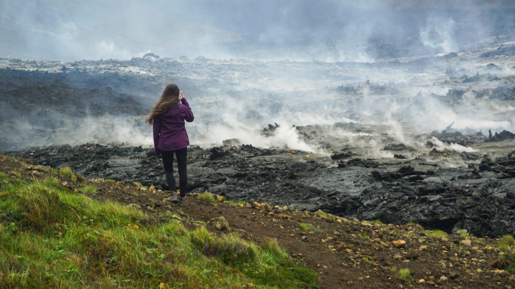A girl in purple jacket standing in front of steaming lava from a recently erupted volcano in Iceland