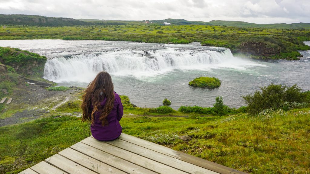A girl in a purple jacket looking at a waterfall that is part of the Iceland road trip itinerary