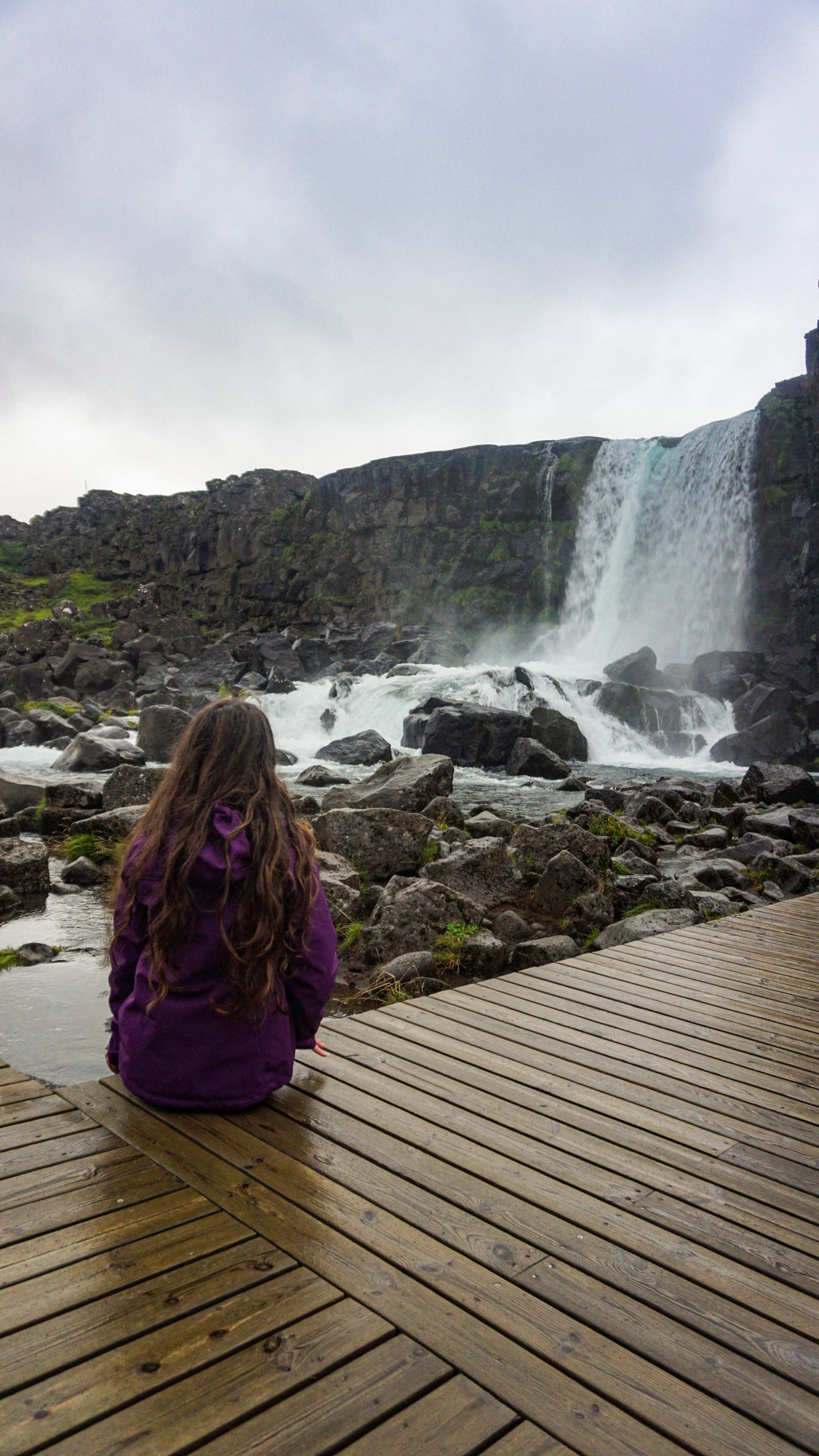 A girl sitting at the foot of a waterfall in Thingvellir National Park