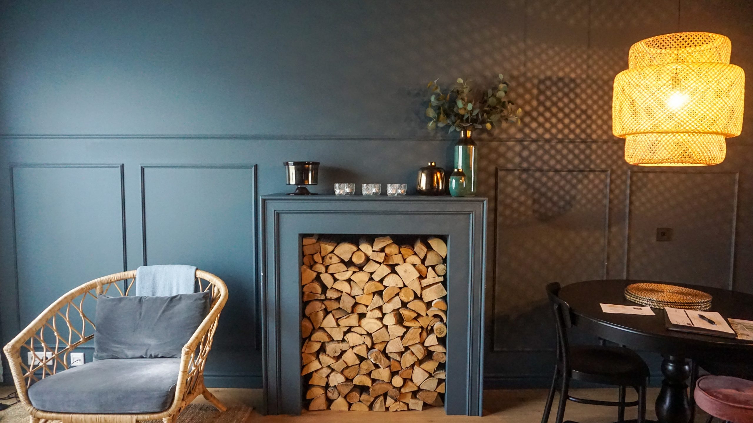 A chair with grey cushions, a fireplaces filled with logs and a black round kitchen table at Inni Boutique Apartments in Iceland