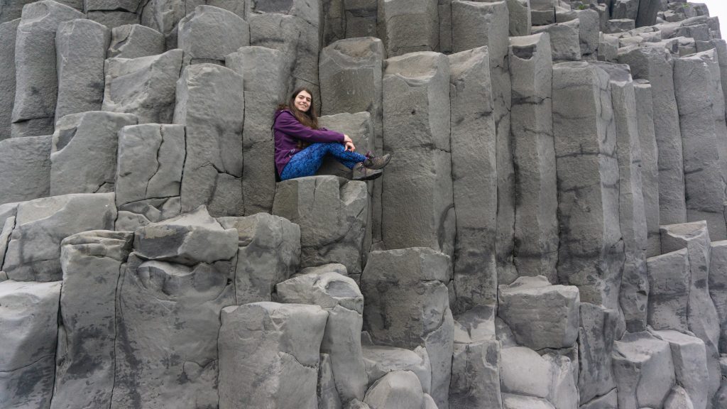 A girl sitting on top some basalt columns at a black beach in Iceland