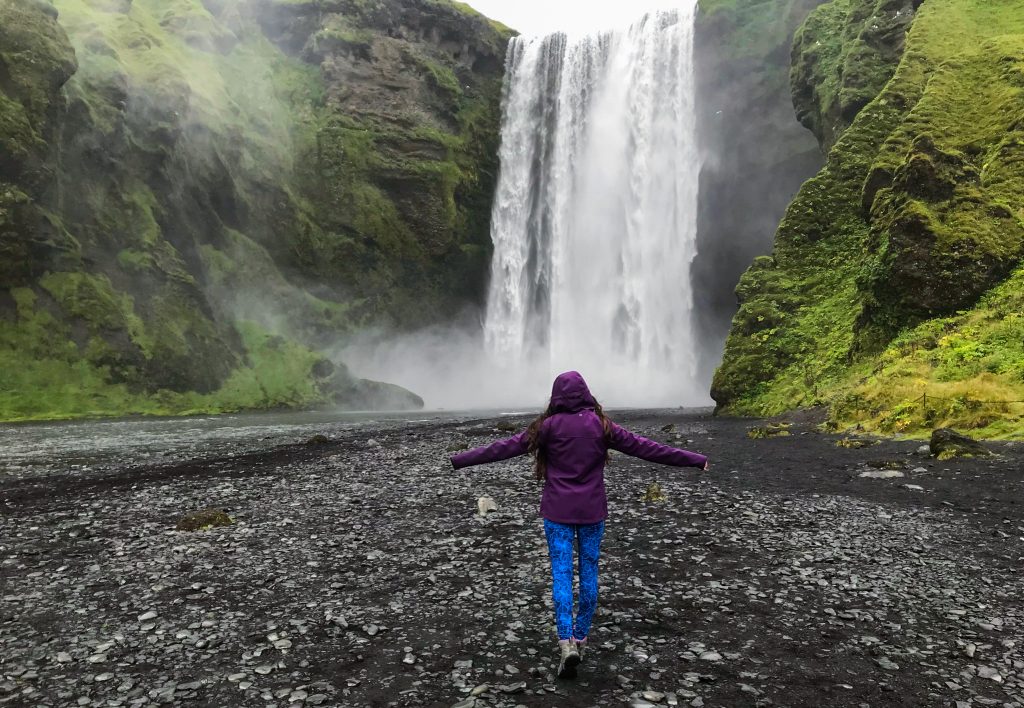 A girl in a purple jacket standing in front of waterfall in Iceland