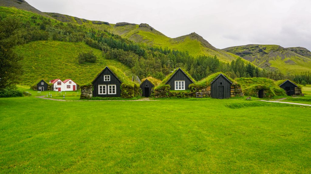 Three houses with a roof covered in grass outside a museum