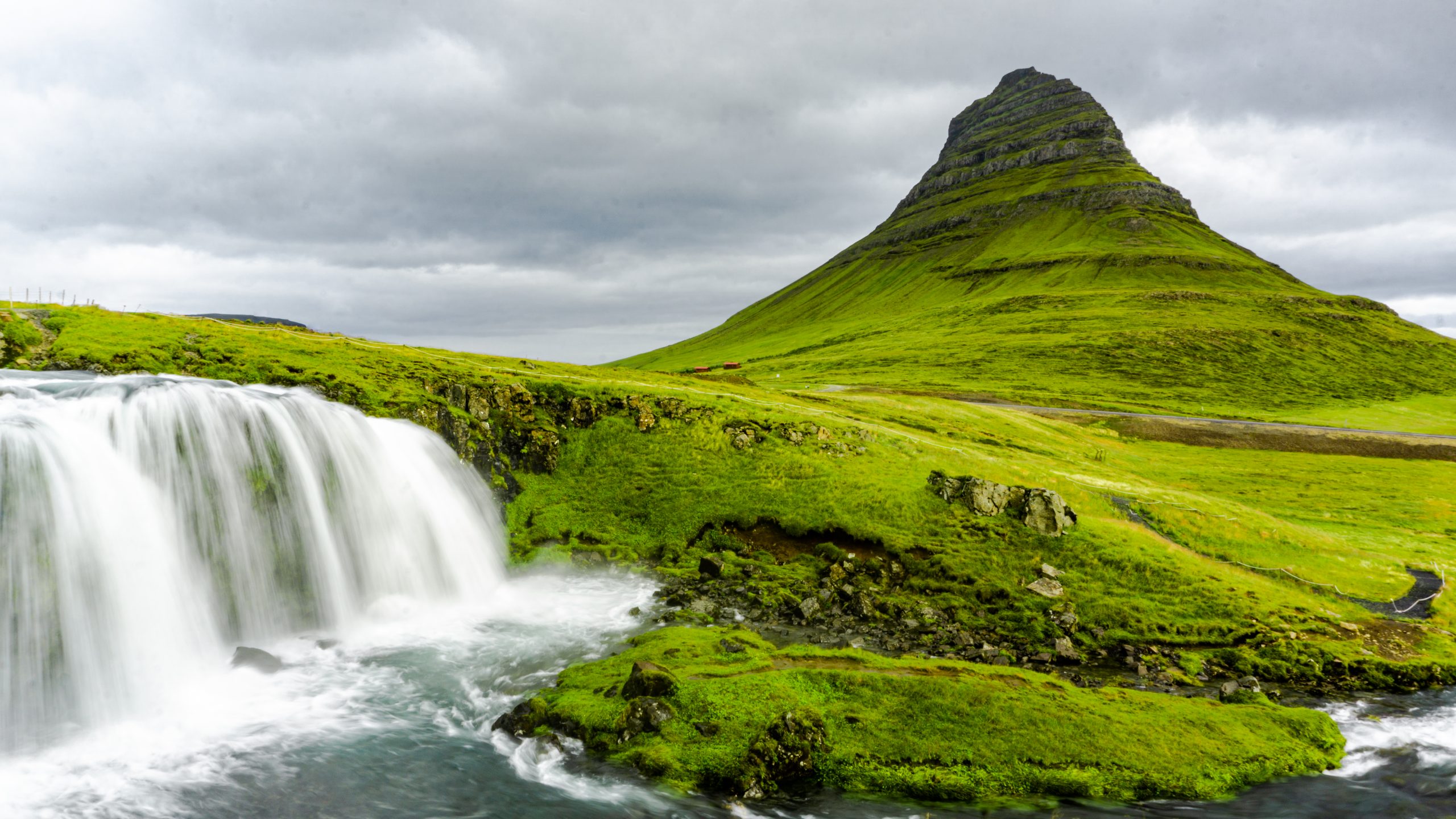 A waterfall in front of a dome-shaped mountain that you can stop on a road trip to Iceland