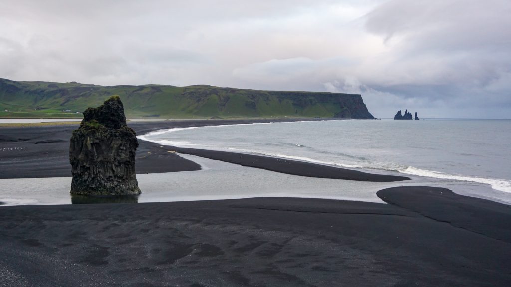 View of a black sand beach from the top of a cliff in Iceland while following a road trip itinerary